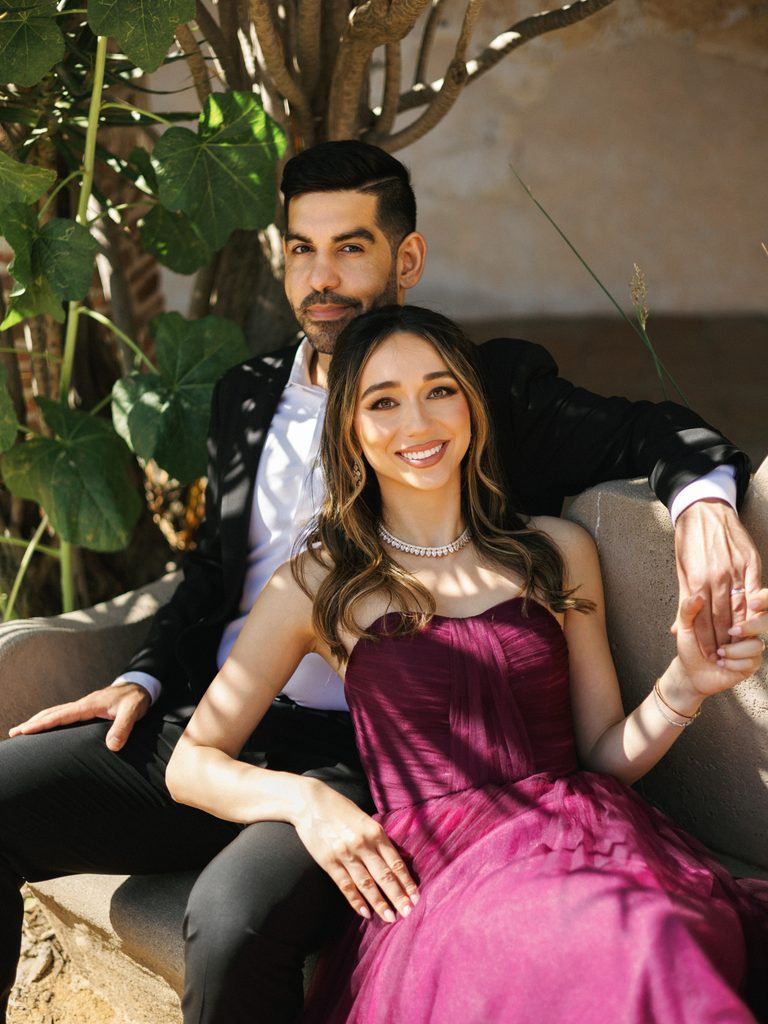 Bride-to-be in a burgundy tulle dress sitting on a bench with her fiancé, inspiring formal engagement photo outfits.