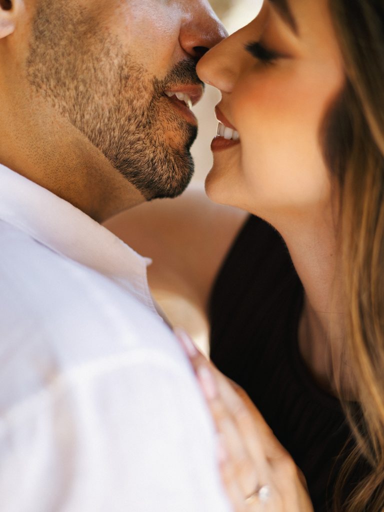 Man with a beard smiling intimately close to a brunette woman's face during an outdoor photoshoot.