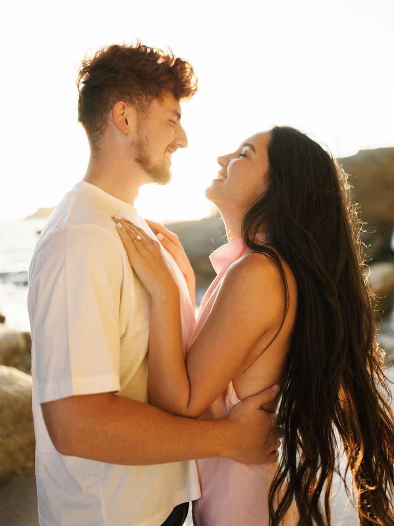 Close-up profile portrait of a couple smiling at each other at sunset, highlighting summer engagement photo outfits.