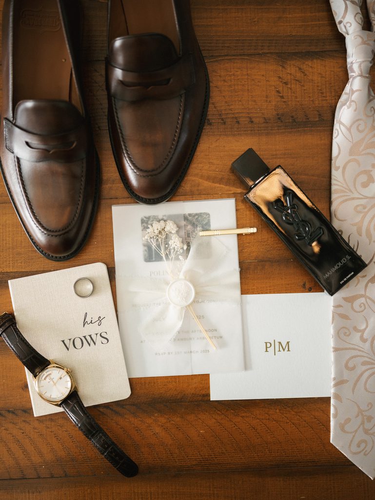 Elegant groom details flat lay on a wooden surface featuring brown leather loafers cologne and his vows booklet