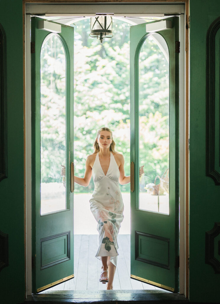 Elegant bride in a silk slip dress walks through tall green double doors of a luxury estate