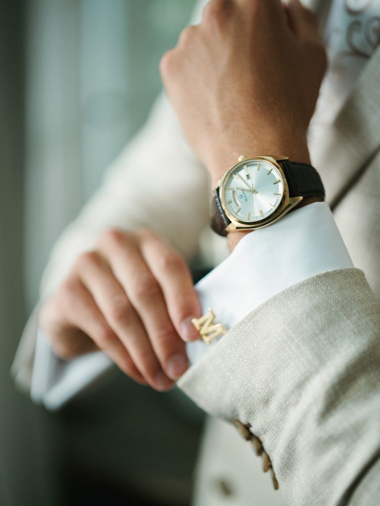 Close up of a groom adjusting his shirt cuff showing off personalized gold monogrammed cufflinks and a luxury watch