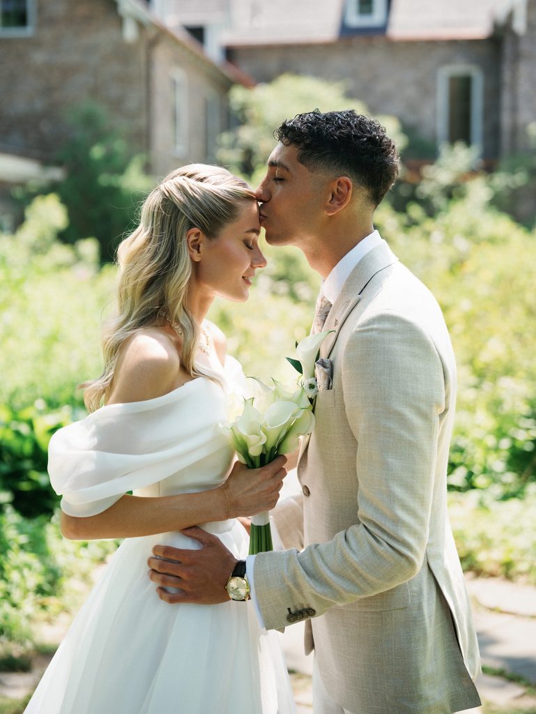 Groom gently kisses the brides forehead during an outdoor portrait session demonstrating romantic wedding photo poses