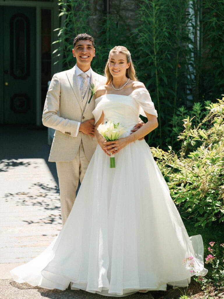 Beautiful bride and groom look at the camera and smile warmly during their outdoor wedding portrait session