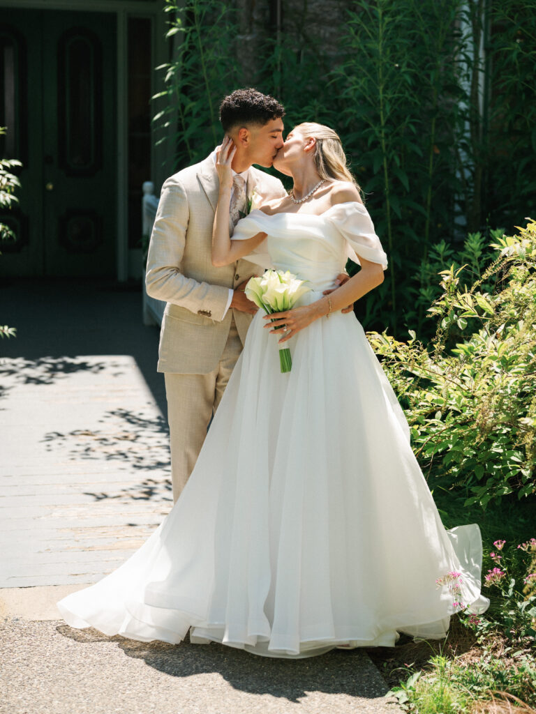 Newlyweds share a romantic kiss in full length while posing in front of a luxury historic estate