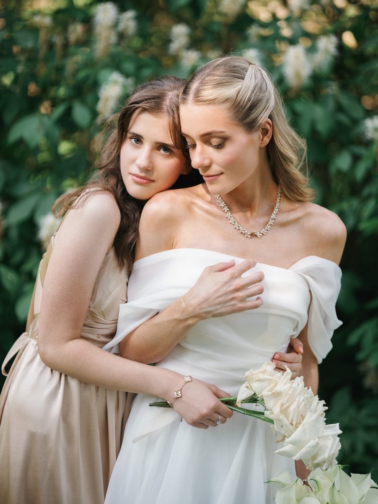 Bride and her maid of honor share a quiet editorial moment highlighting the elegant details of the wedding gown