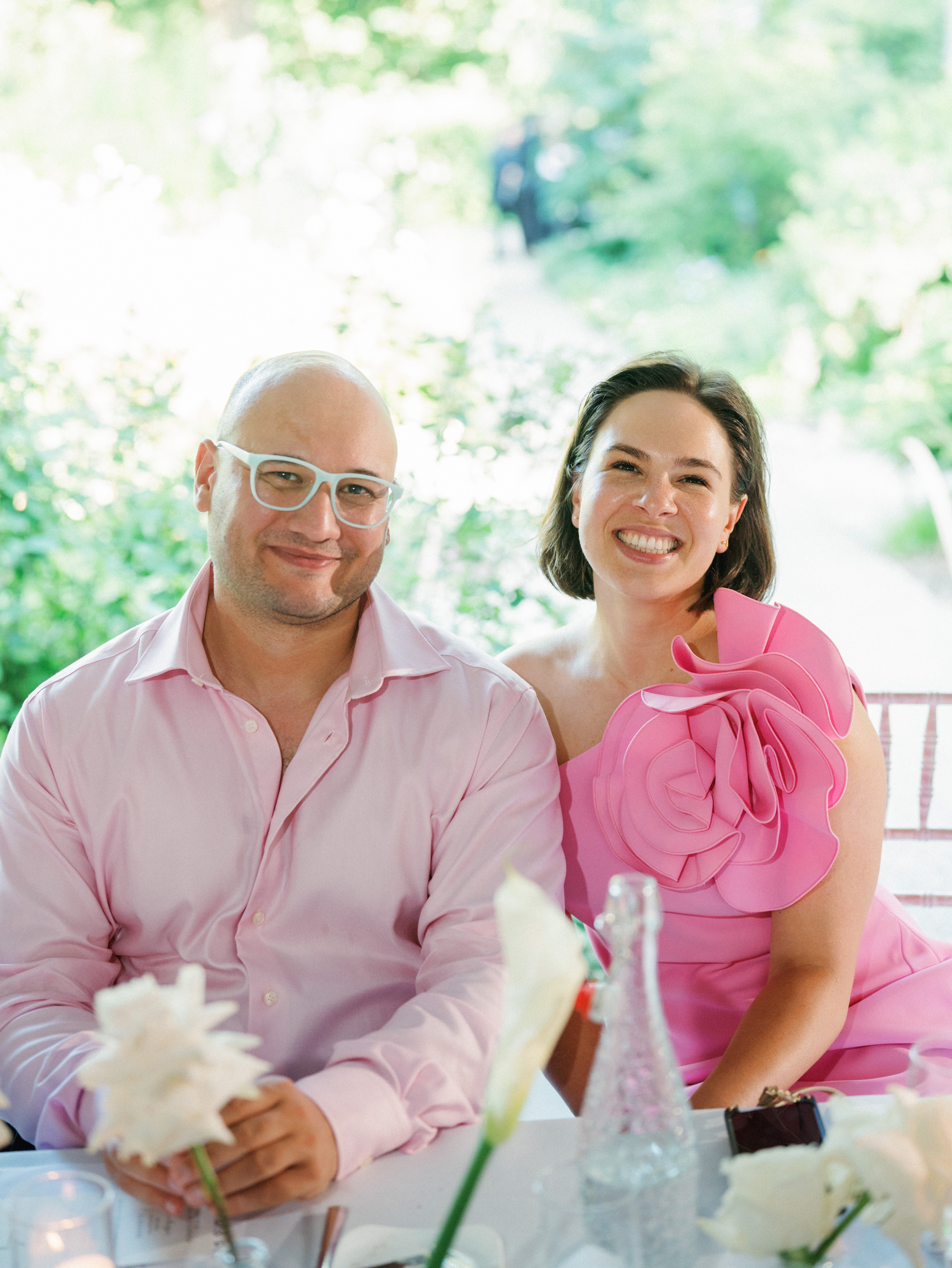 Happy wedding guests smile warmly while seated at an outdoor reception dinner table