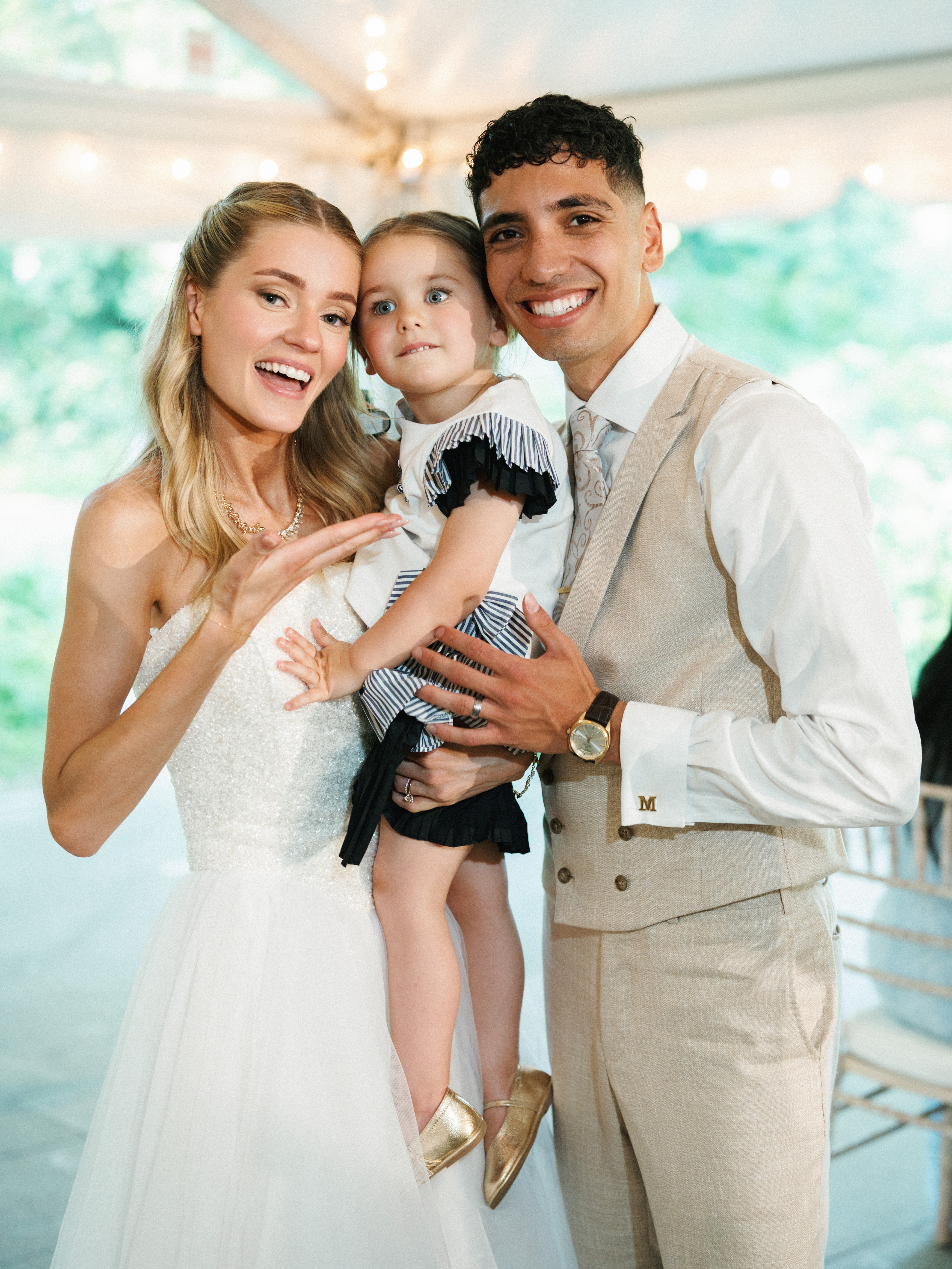 Joyful newlyweds pose together with a sweet flower girl inside an elegant tented reception venue