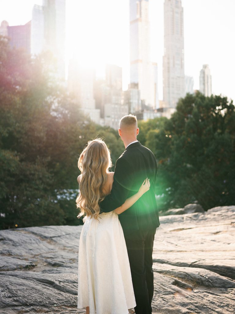 Couple standing on a rocky hill looking at the city skyline, showcasing formal engagement photo outfits.