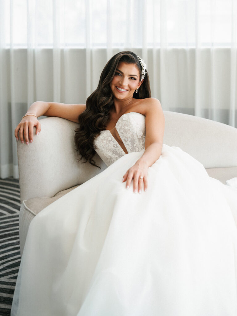 Gorgeous smiling bride posing in a strapless ballgown on a chic armchair showcasing timeless coverage included in a wedding photographer contract