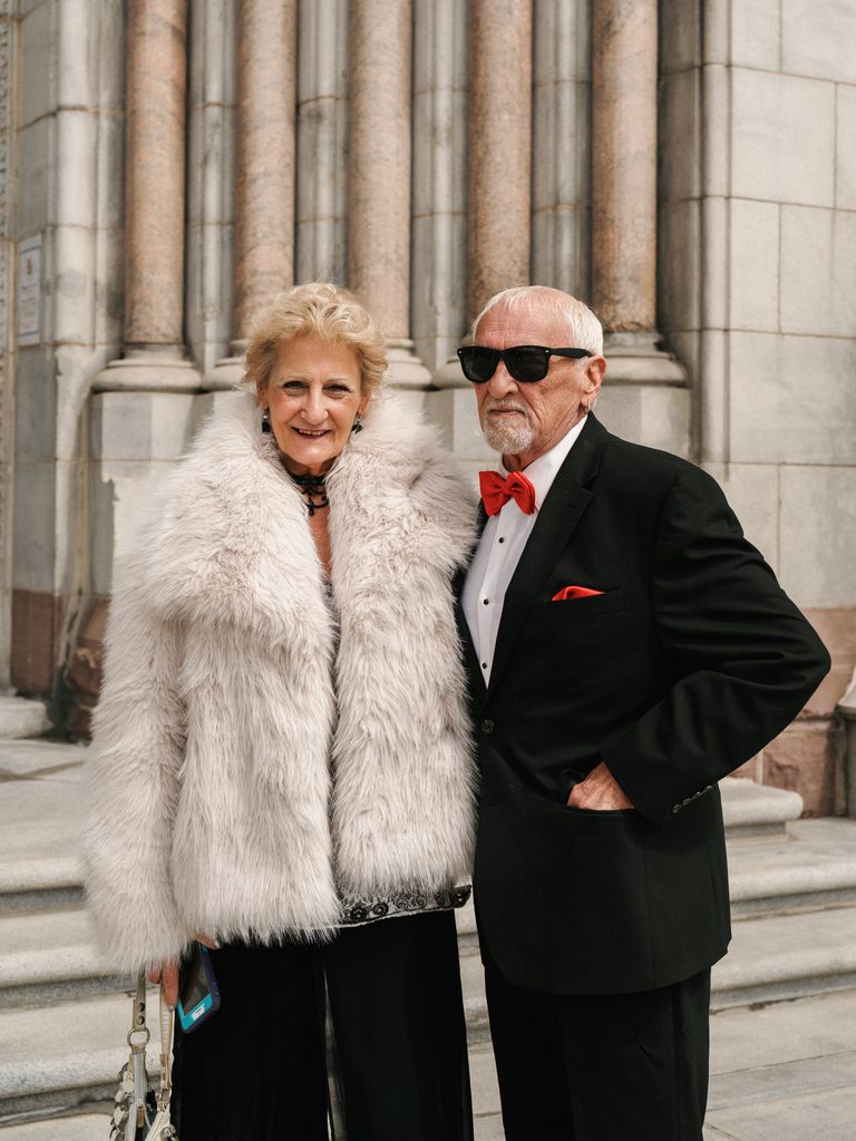 Sophisticated senior wedding guests in a luxury fur coat and black tuxedo with a red bow tie