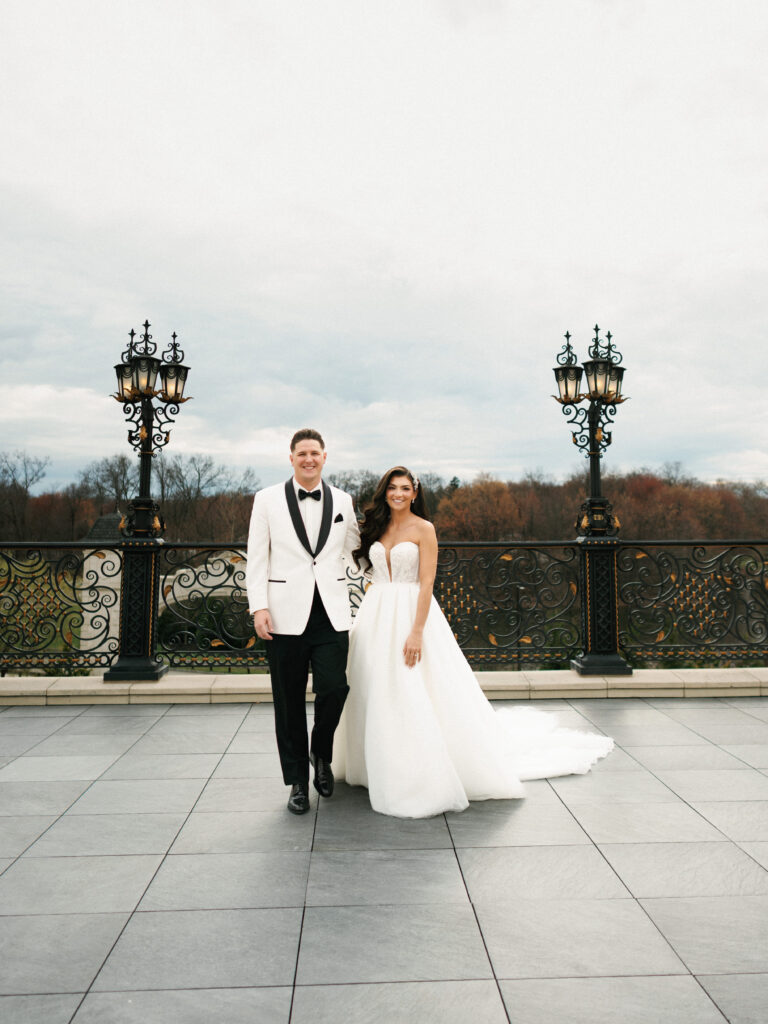 Wide angle shot of a wealthy couple walking on a grand stone terrace with historic black iron lanterns and scenic background view