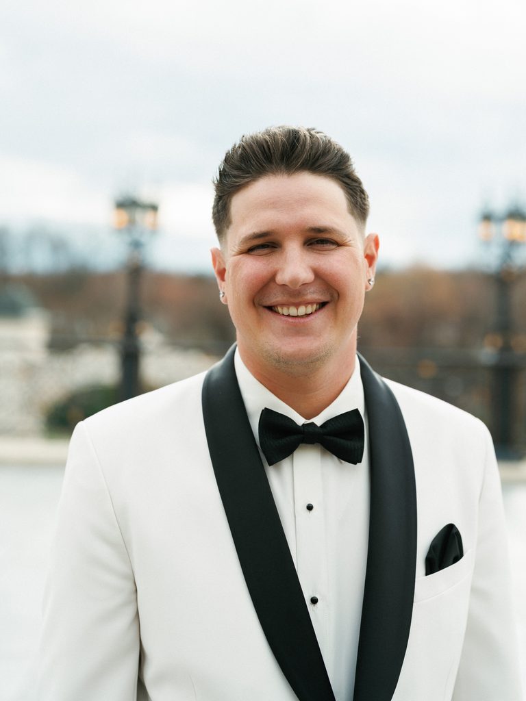 Handsome smiling groom posing outdoor in a luxury white tuxedo jacket with a classic black silk bow tie