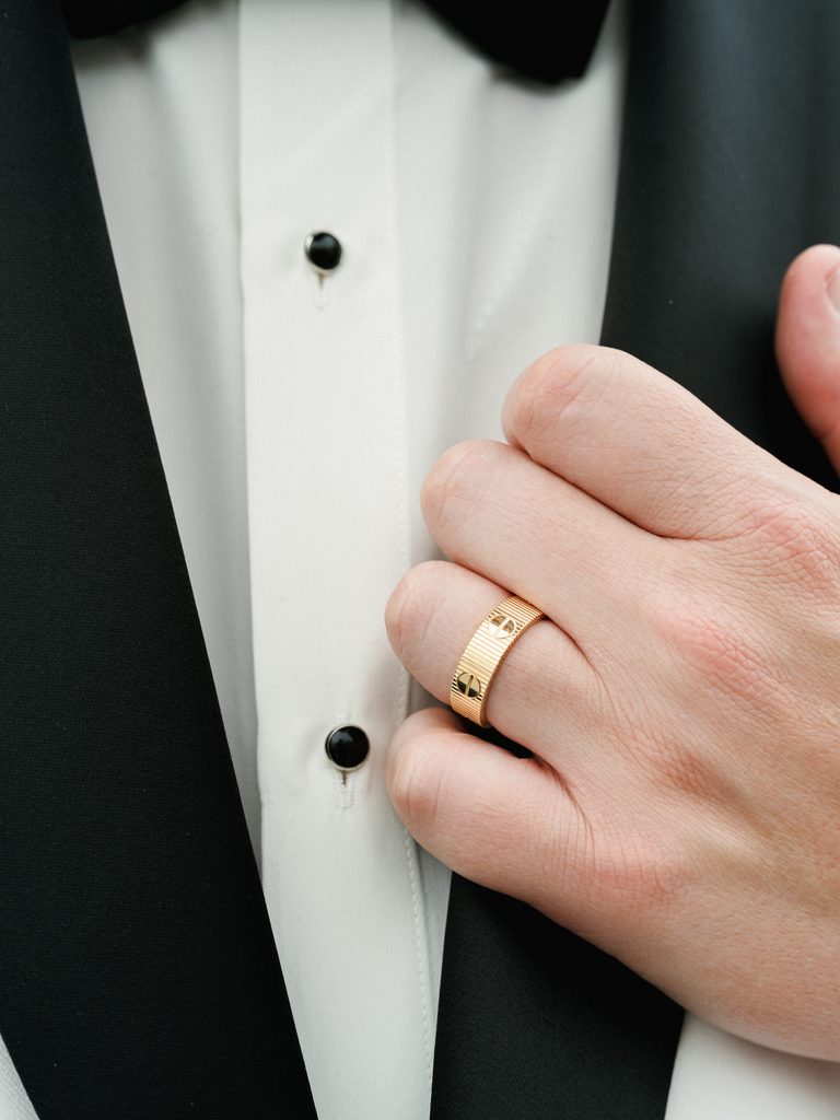 Close up of a grooms hand wearing a luxury gold cartier love wedding ring on a white tuxedo shirt covered by a professional wedding photographer contract