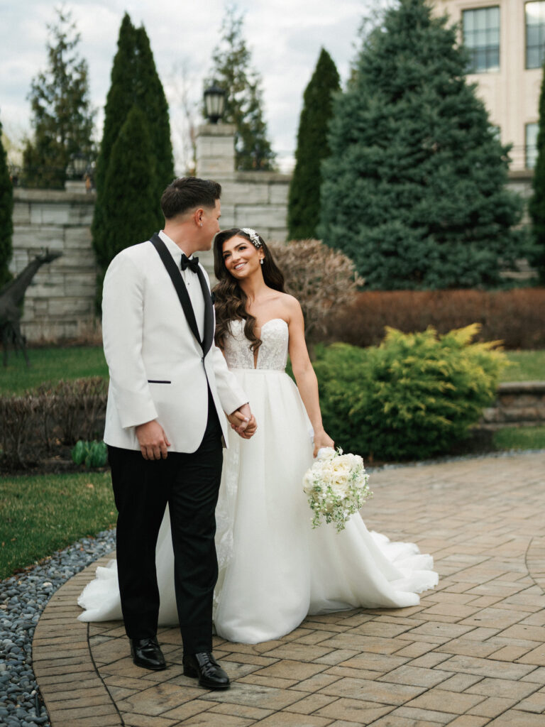 Candid destination wedding couple walking hand in hand outdoor with a classic white tuxedo jacket and a line bridal gown covered by a trusted wedding photographer contract