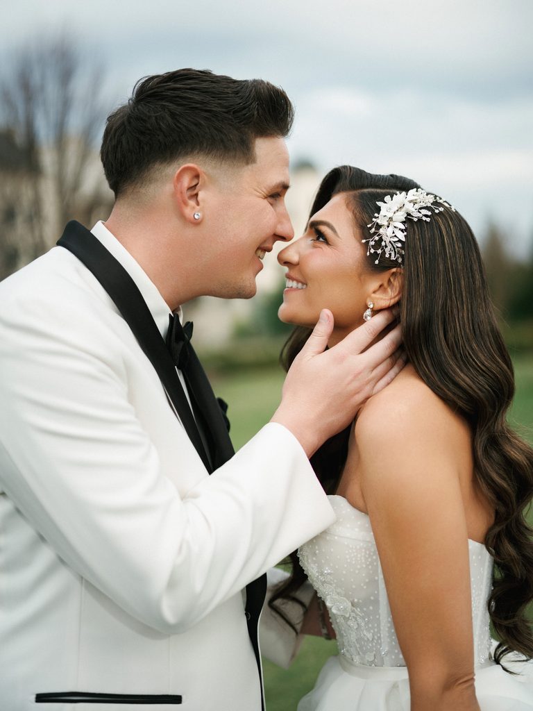 Intimate outdoor couple portrait with a groom gently touching bride face showing elegant hollywood waves hairstyle and white tuxedo jacket