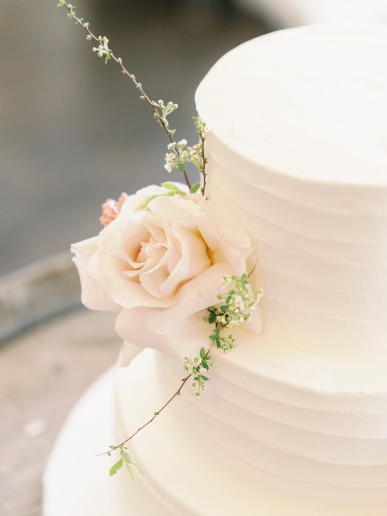 Close-up of a tiered white wedding cake decorated with elegant fresh roses for a wedding photo gallery. 
