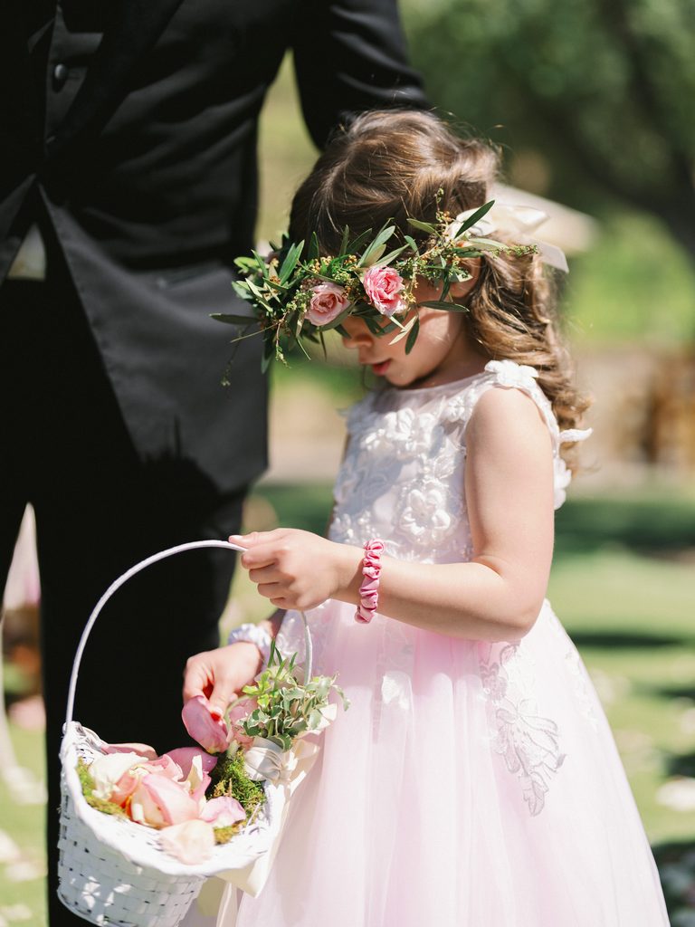 Little flower girl wearing a pink rose crown and holding a white basket of petals.