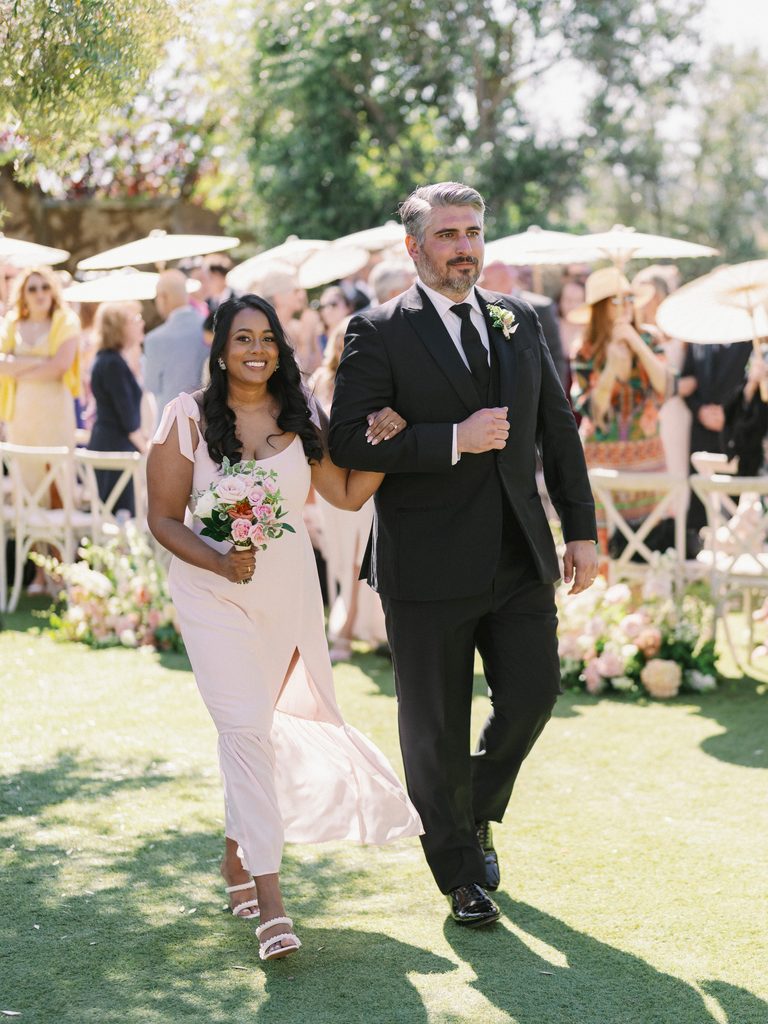 Groomsman and bridesmaid in a blush dress arm-in-arm, captured for a luxury wedding photo gallery.