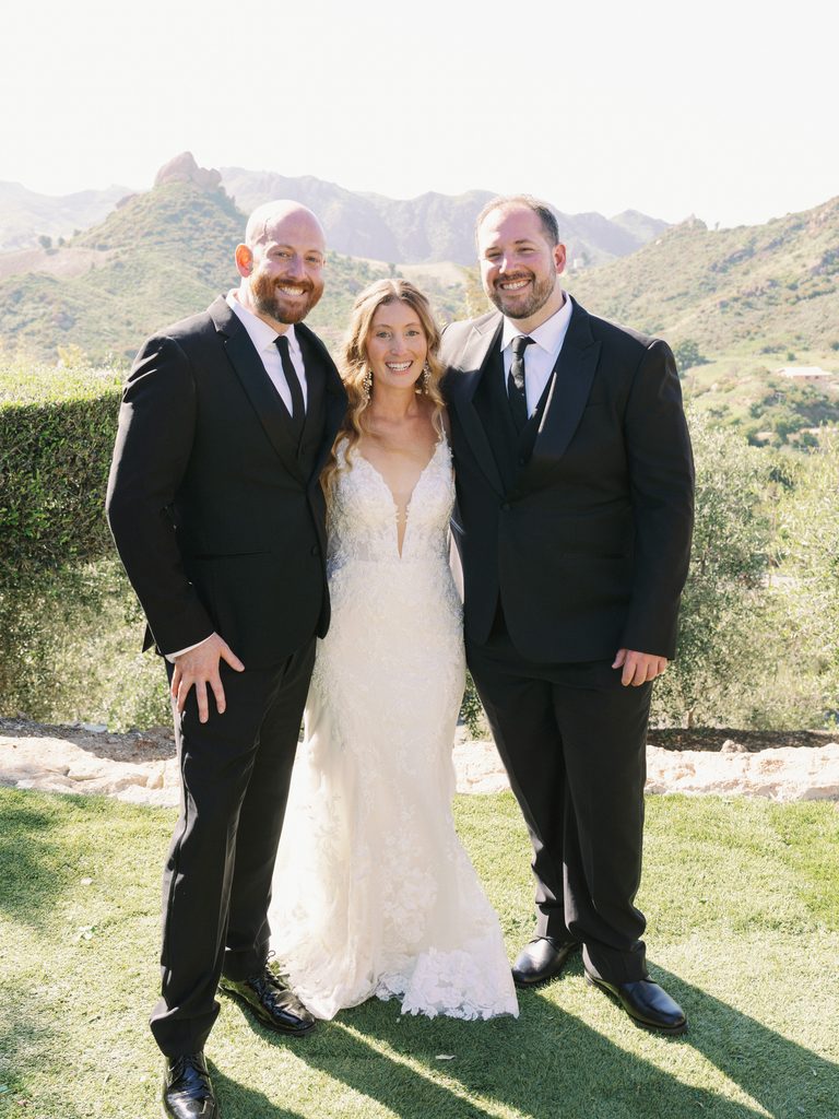 Newlyweds smiling while posing with a groomsman during an outdoor reception session.