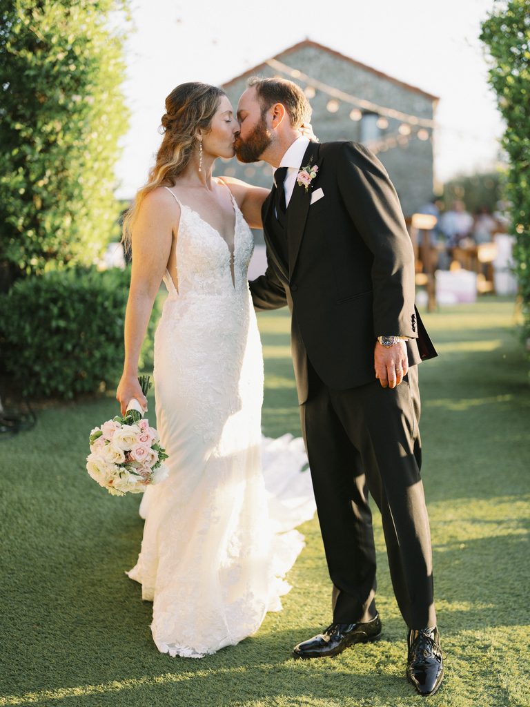 Newlyweds sharing a romantic kiss on a sunny lawn at their outdoor venue.