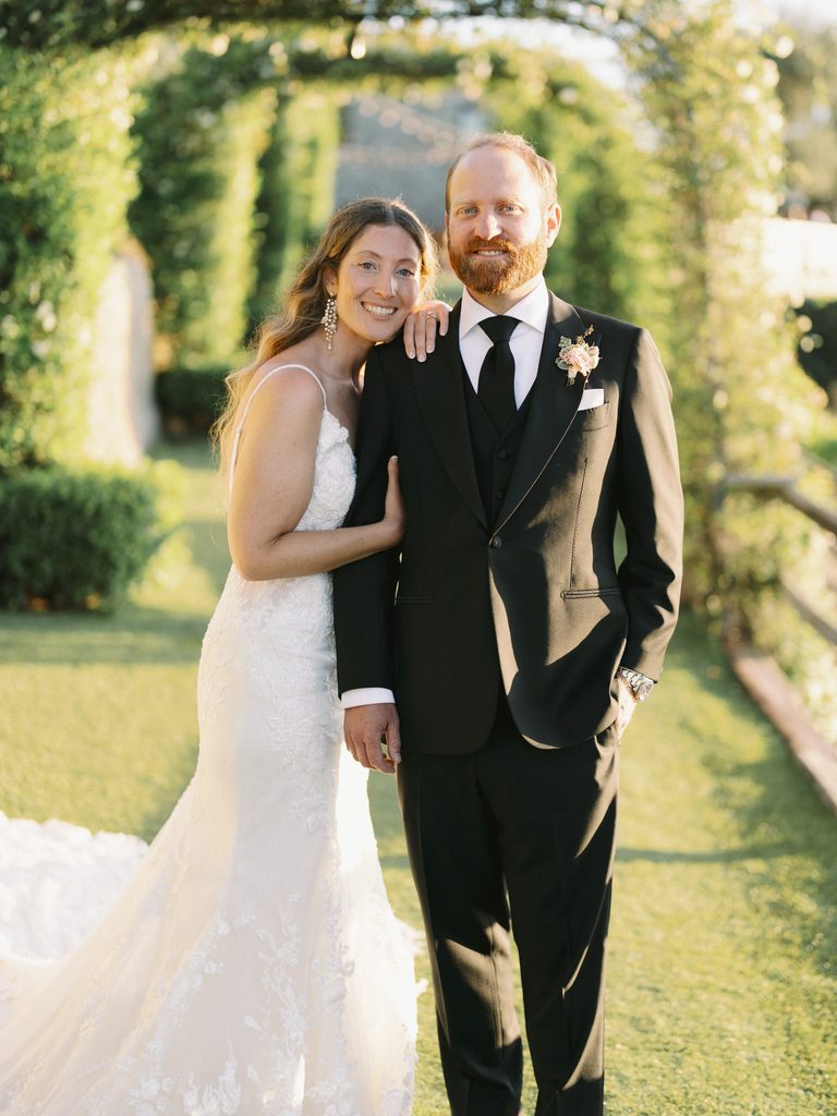 Bride leaning on her groom's shoulder under the glowing sunset light in a garden.