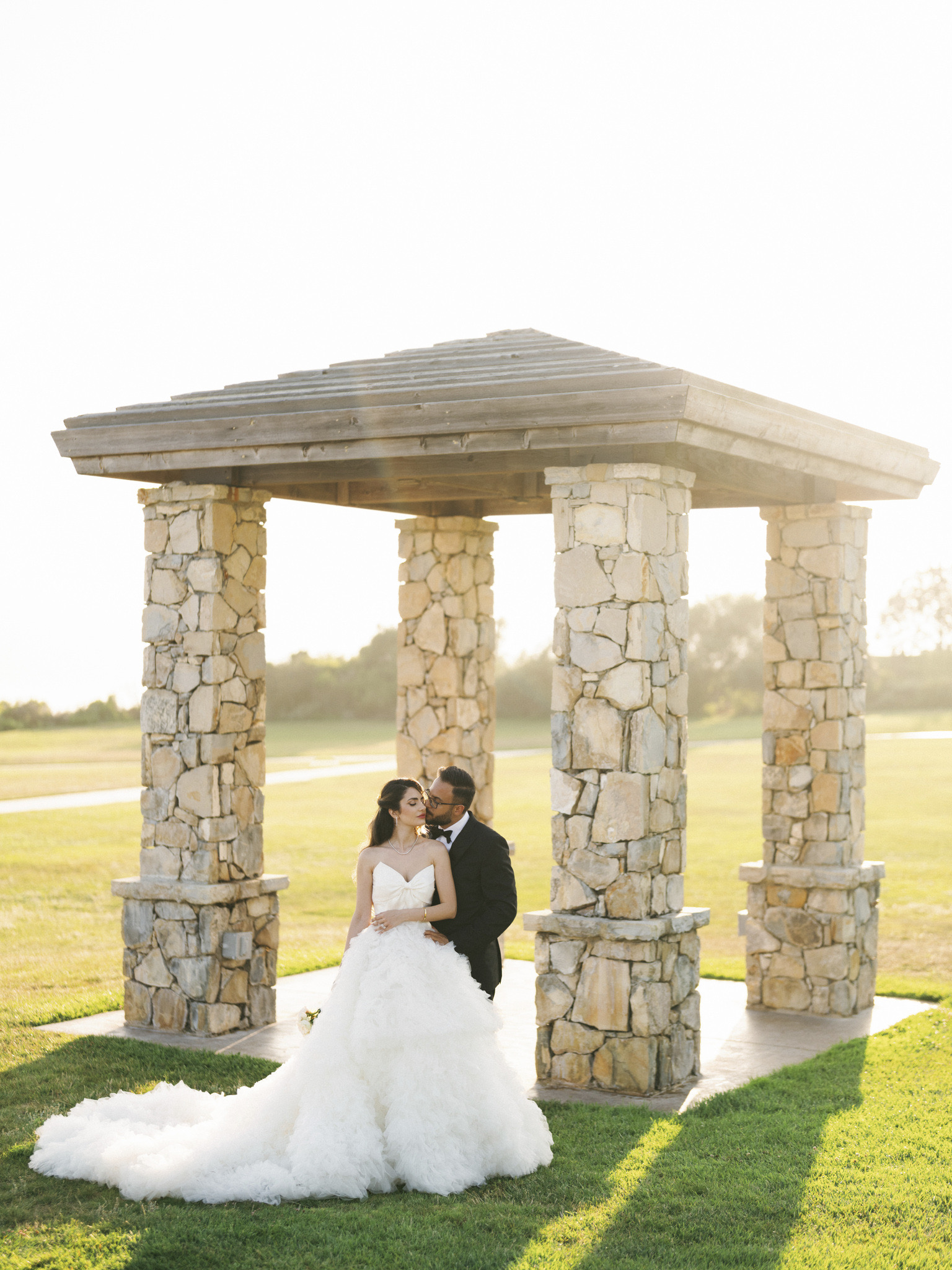 Couple kissing beneath a stone pavilion.