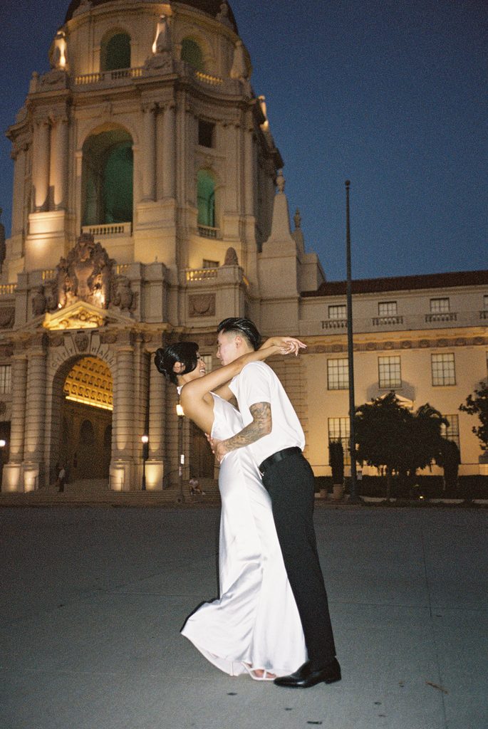 Modern newlyweds posing near beautiful city tower architecture for blue hour wedding photos