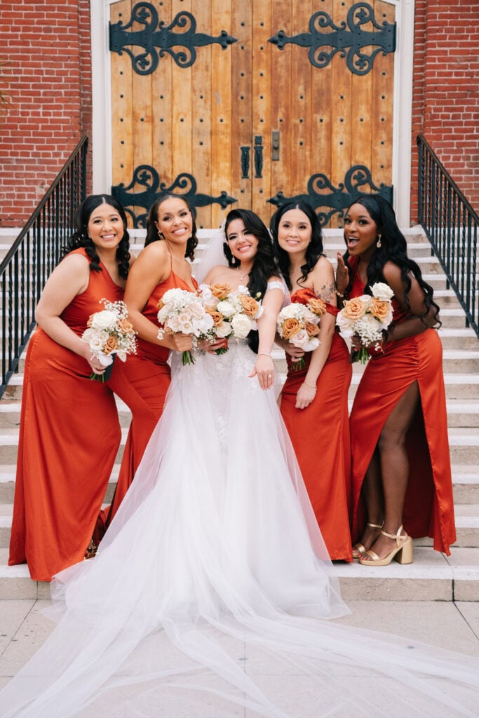 A bride showing off her wedding ring to her bridesmaids in matching orange dresses, while the groom smiles warmly behind them. A behind-the-scenes look at a joyous celebration, with seamless wedding planning by Not Jess A Planner and photography by Dreamwood Photo.