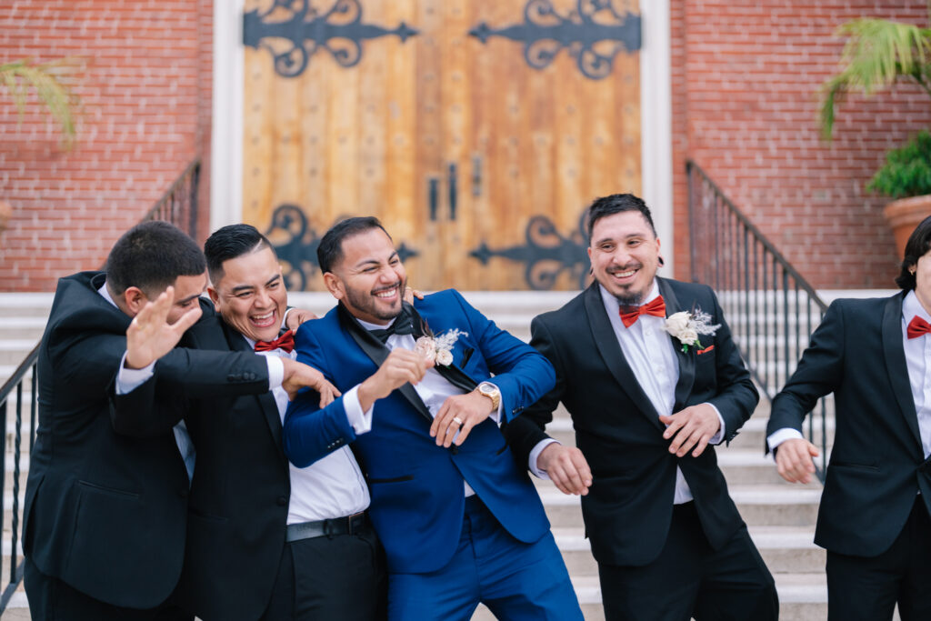 The groom in a striking blue suit laughing and celebrating with his groomsmen in black tuxedos. A candid, high-energy moment from a California wedding celebration, beautifully documented by Dreamwood Films and coordinated by Not Jess A Planner.