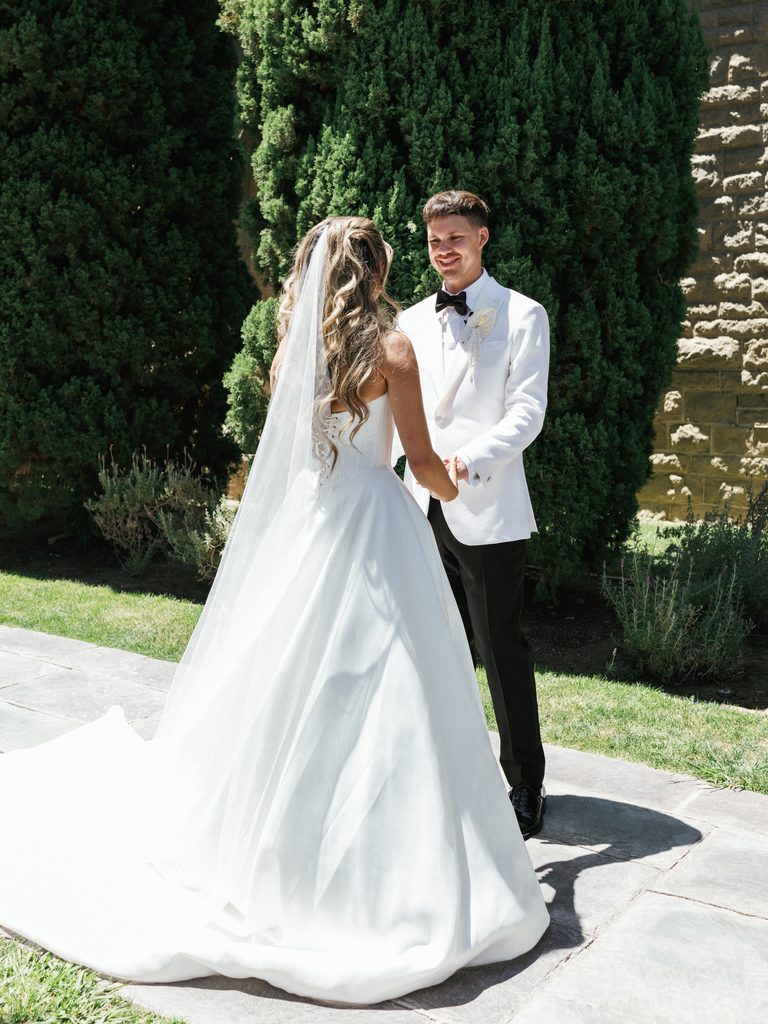 Elegant bride back view showing long tulle veil while holding hands with groom outdoors