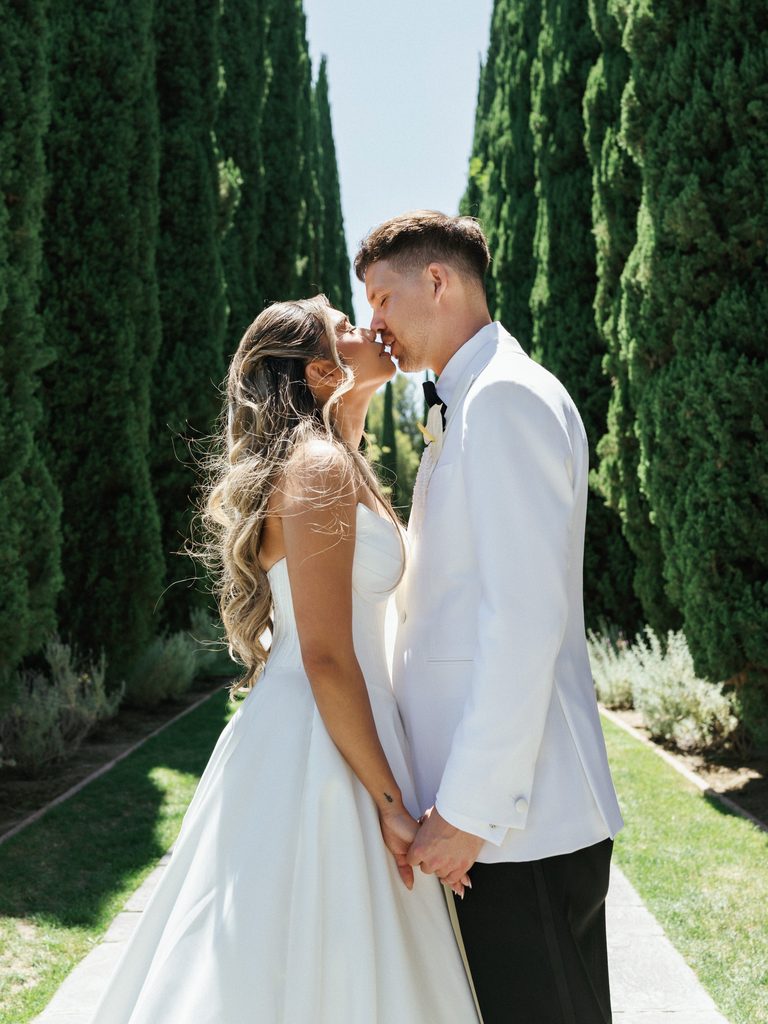 Close up profile portrait of newlyweds sharing a sweet kiss outdoors in bright sunlight
