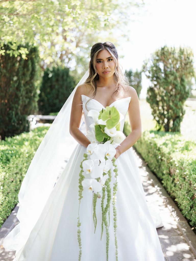 Stunning brunette bride portrait featuring modern sweetheart neckline dress and lush exotic greenery bouquet