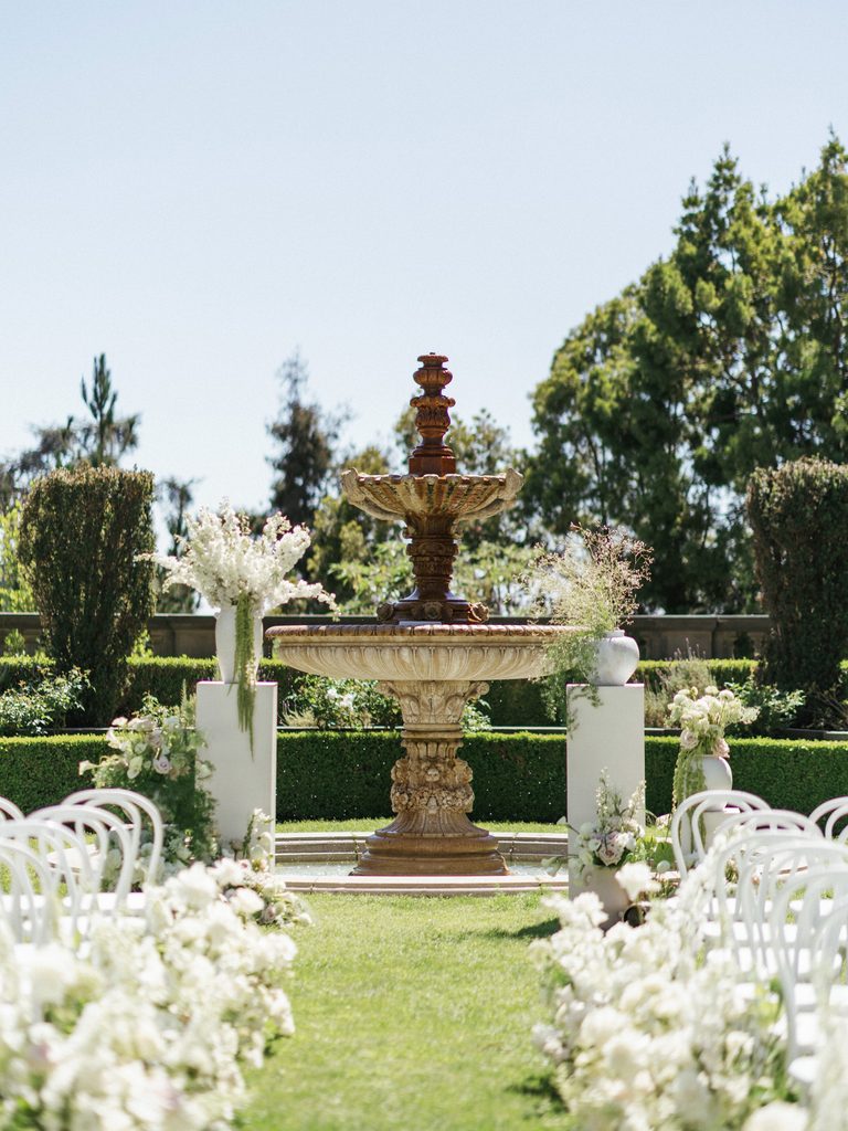 Luxury garden ceremony venue location with lush white floral arrangements lining the aisle green grass