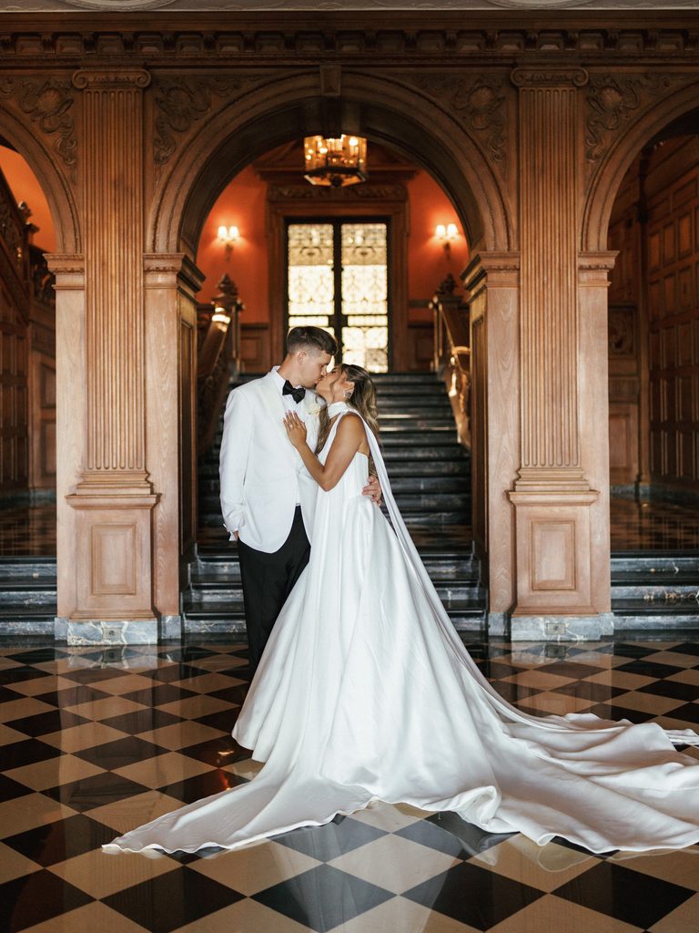 Romantic bride and groom kissing on checkered black and white floor of luxury estate