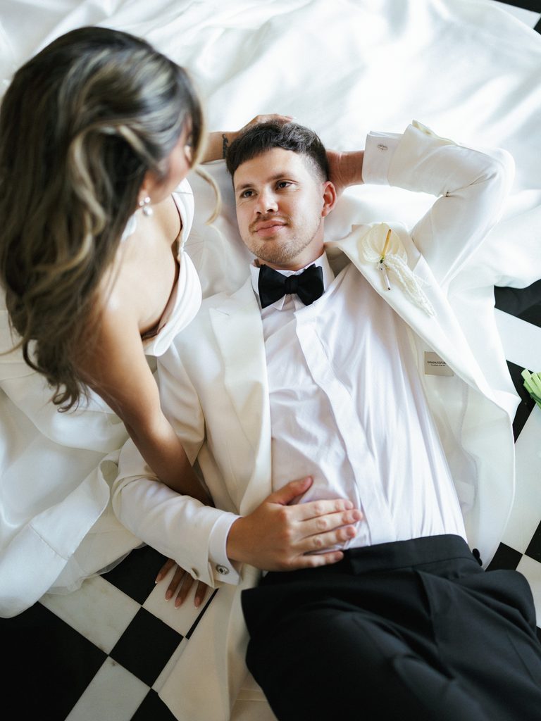 High angle view of groom lying on checkered black and white floor looking up at bride