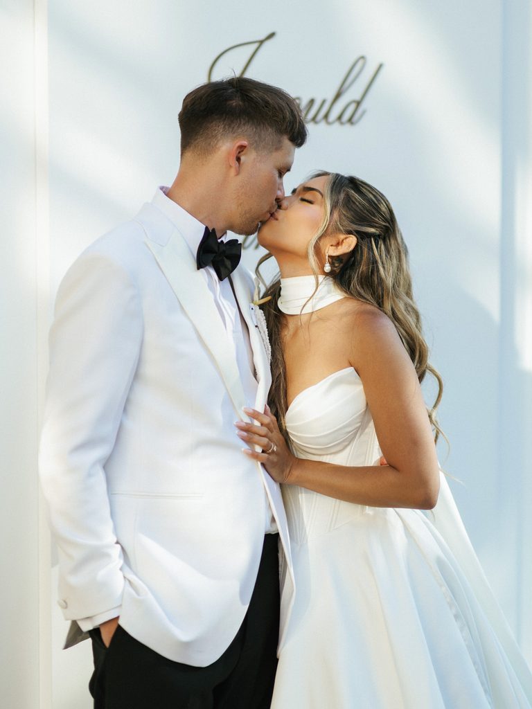 Beautiful newlyweds sharing a sweet kiss against white wall background during indoor portrait session