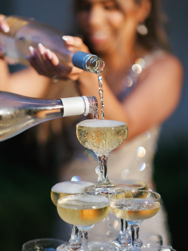Detailed texture of prosecco pouring into glass pyramid with smiling bride blurred in background