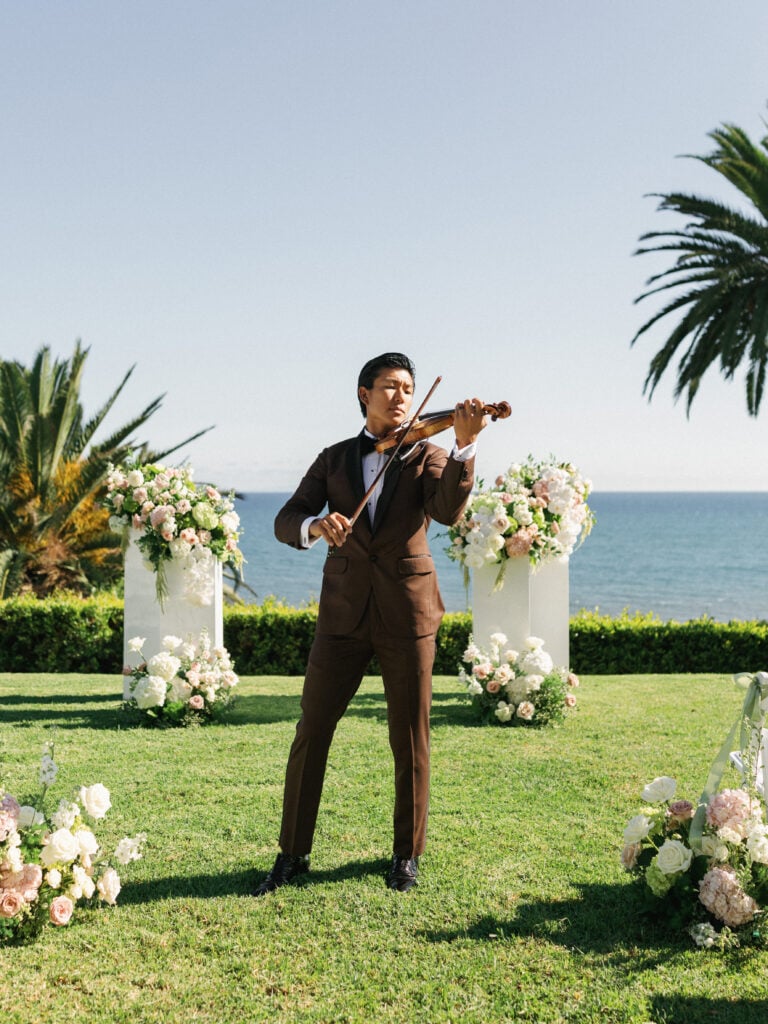 Talented violinist playing music outdoors during luxury wedding ceremony overlooking the ocean