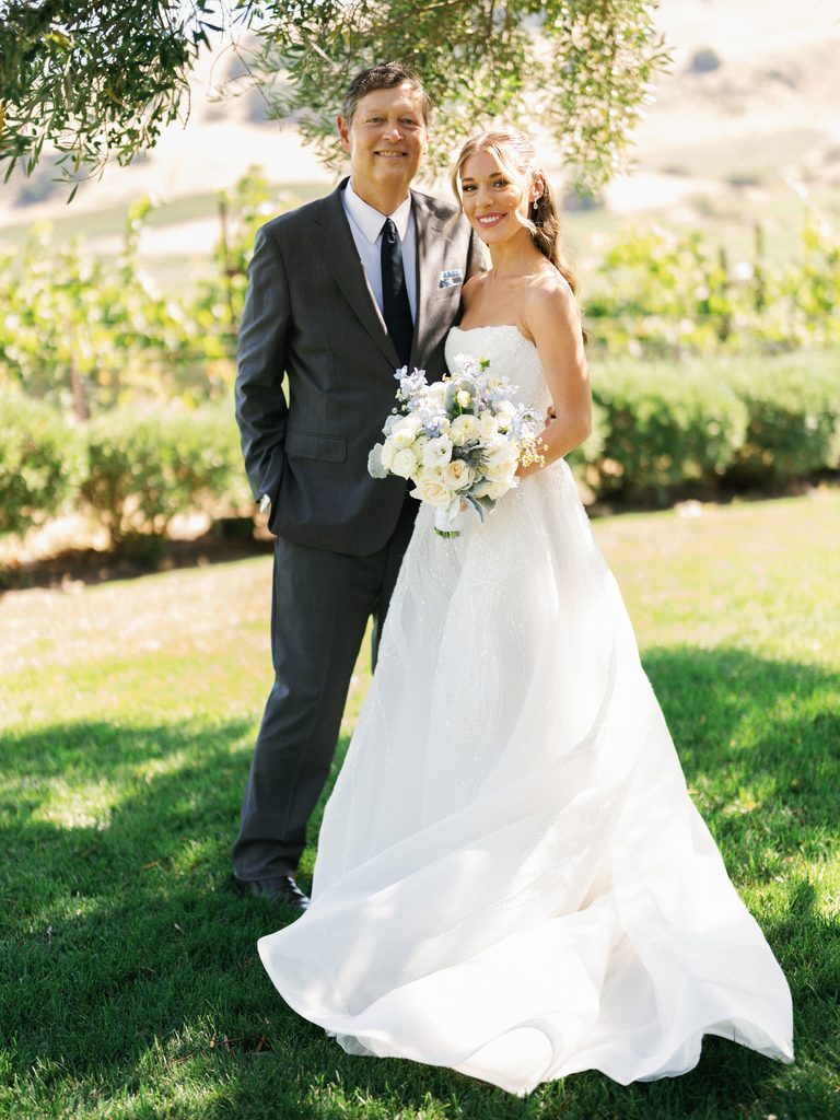 Smiling bride posing with her father on green grass at upscale vineyard estate