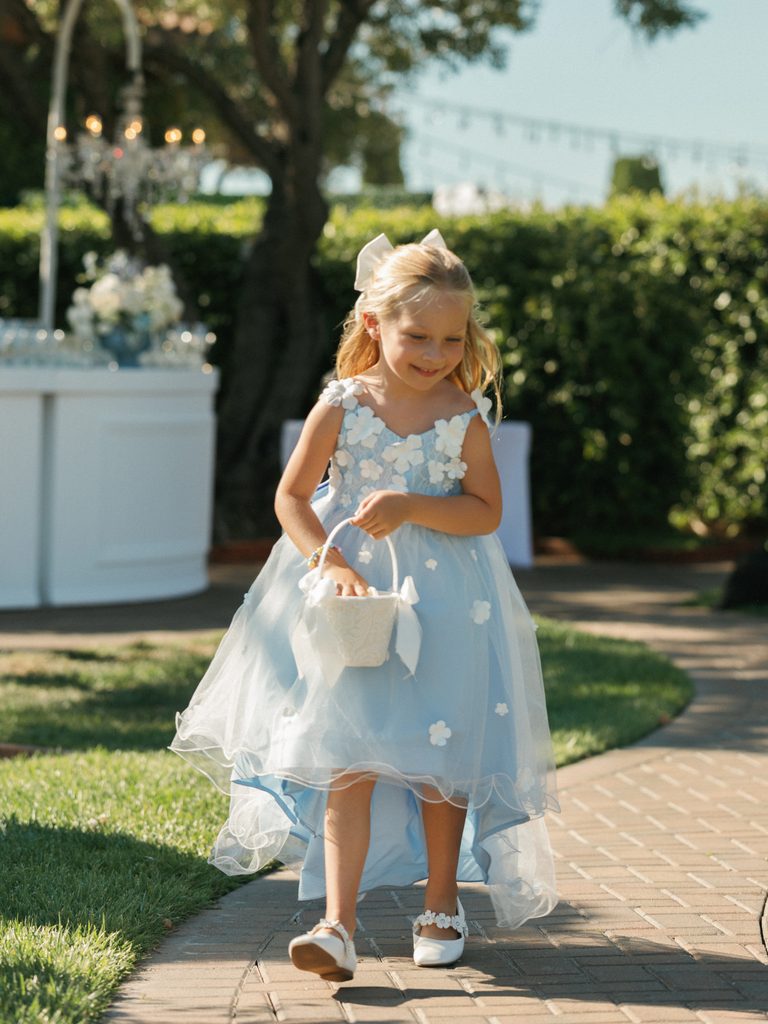 Cute flower girl in blue dress holding basket walking down the aisle at luxury wedding