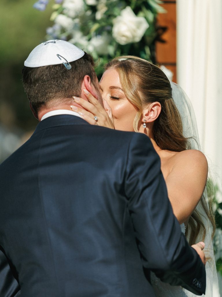 Romantic first kiss moment during luxury jewish wedding ceremony under floral arch