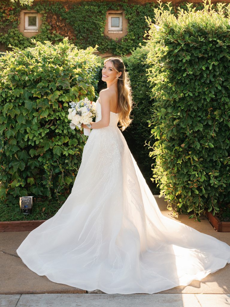 Back view of smiling bride showing long train of luxury wedding gown at vineyard estate