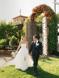 Newlyweds holding hands and walking on green lawn at luxury Viansa Winery wedding venue