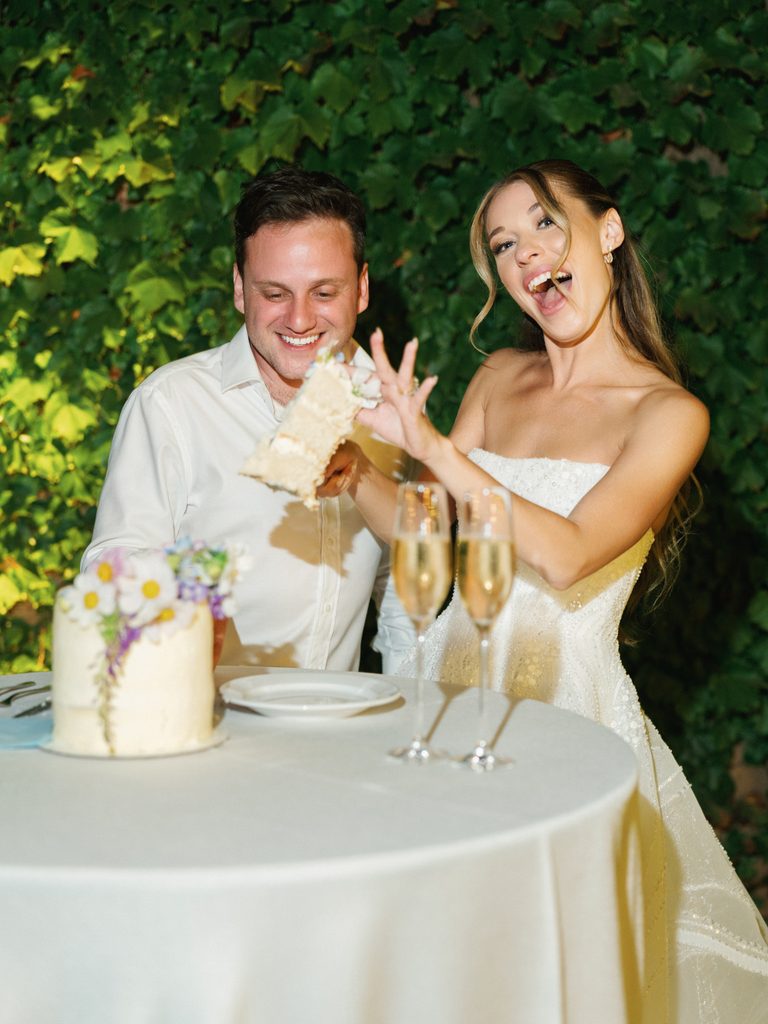 Funny newlyweds cutting cake during luxury outdoor evening wedding reception