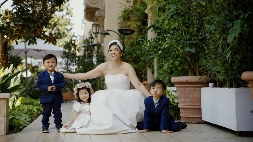 Gabrielle laughing and posing with her flower girl and two ring bearers on a garden path in Orange County. Dreamwood wedding photography