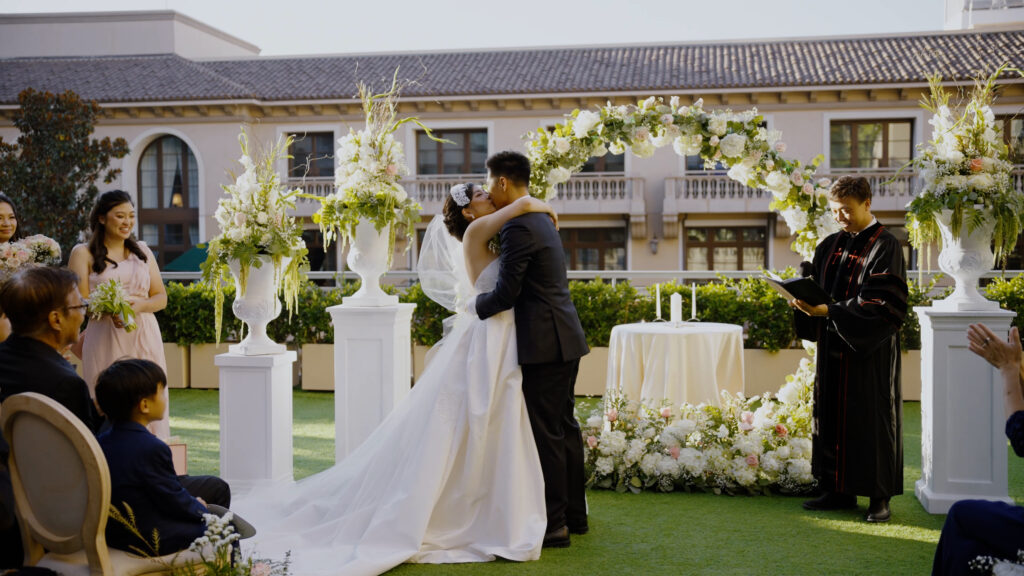 Newlyweds under a white floral arch at their wedding ceremony at The Maybourne Beverly Hills, coordinated by Stephy's Bride Guide.