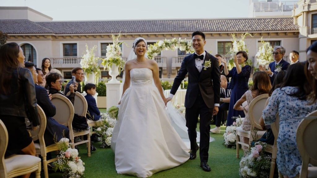 Gabrielle and Nathan smiling as they walk back down the aisle at The Maybourne Beverly Hills, holding hands while guests clap and take photos. Dreamwood wedding photography.
