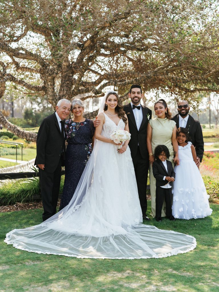 Elegant wedding group photo featuring happy newlyweds surrounded by family members in black tie attire