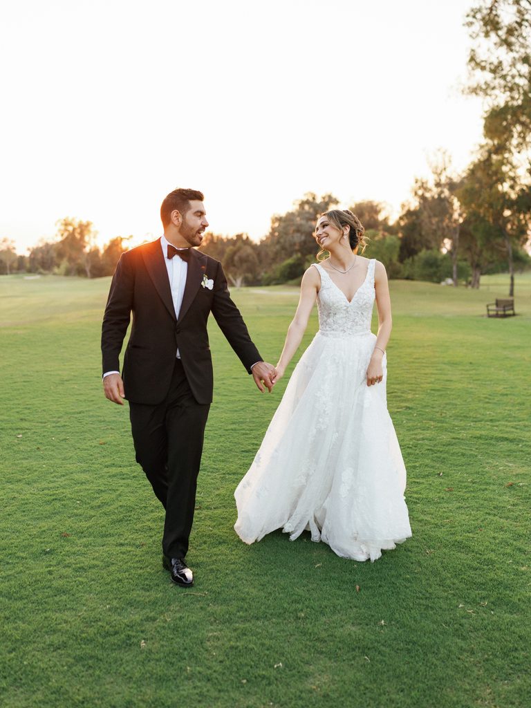 Full length wedding portrait of newlyweds strolling outdoors against beautiful sunset sky